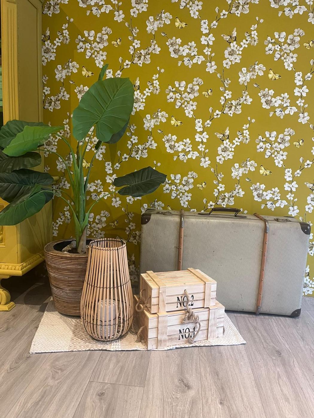 Sfeerhoek in de praktijk met planten, een lantaarn en oude koffers voor een gele bloemenwand